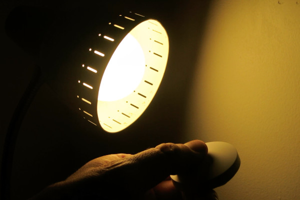 A bedside lamp illuminated to 5%, with a hand holding a Zigbee button in front of it.