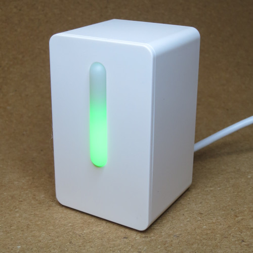 A VINDRIKTNING unit, a white cuboid device with a semi-transparent strip on the front glowing green. 
